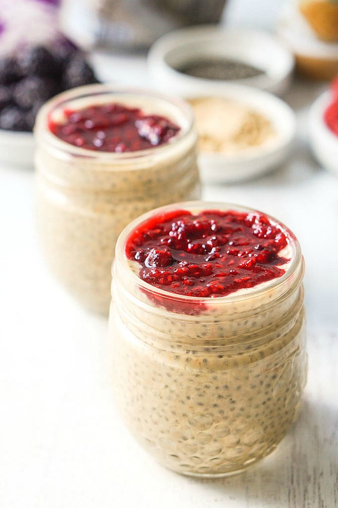 Long photo of 2 jars with peanut butter chia pudding and jelly topping with berries in background.