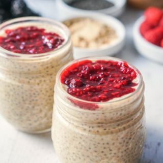 2 jars with peanut butter chia pudding and jelly topping with berries in background.