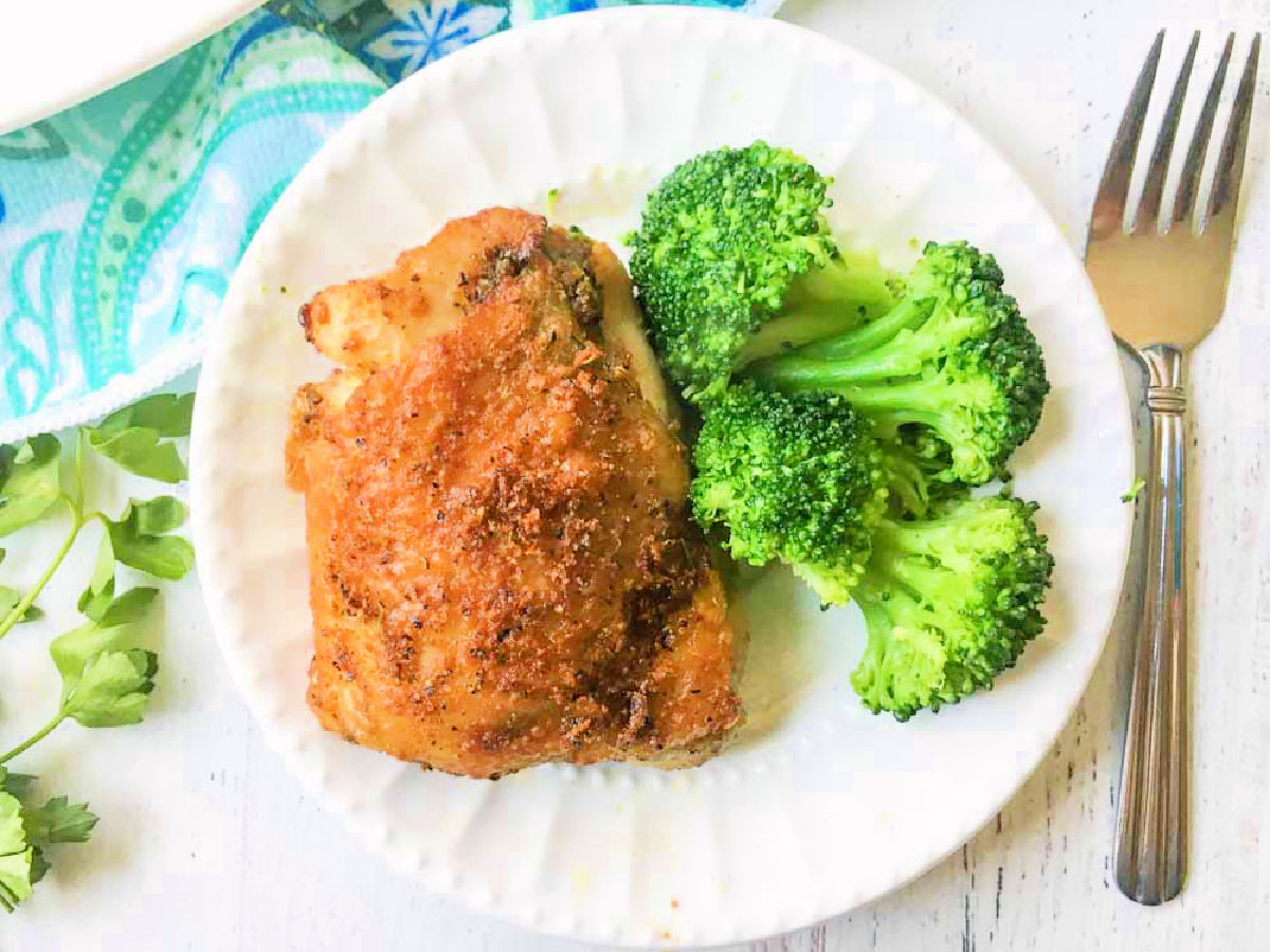 aerial view of white plate with chicken thigh and broccoli