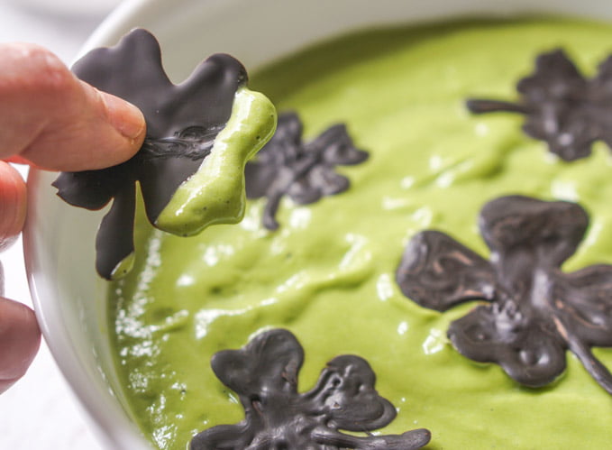 Closeup of chocolate shamrock dipped in green smoothie bowl.