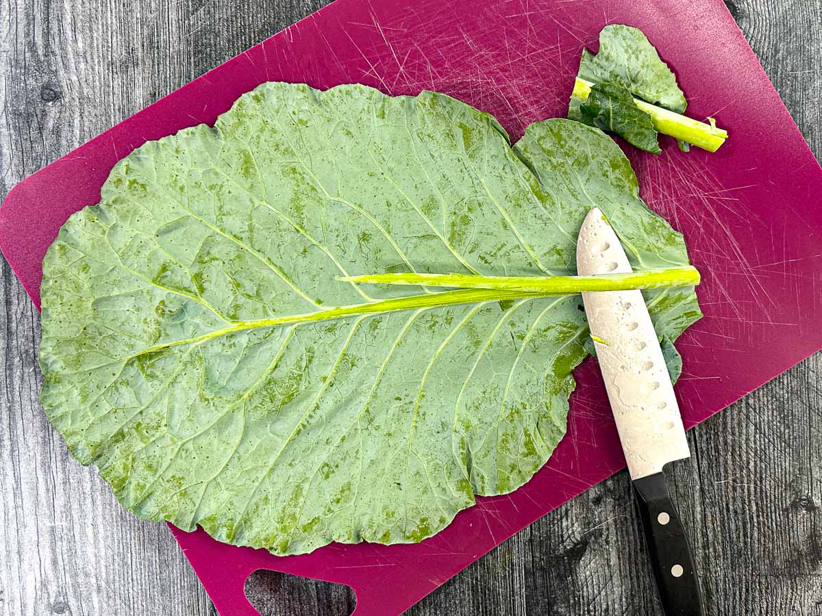 A purple cutting board with a big collard green and a knife showing how to prepare the wraps. 