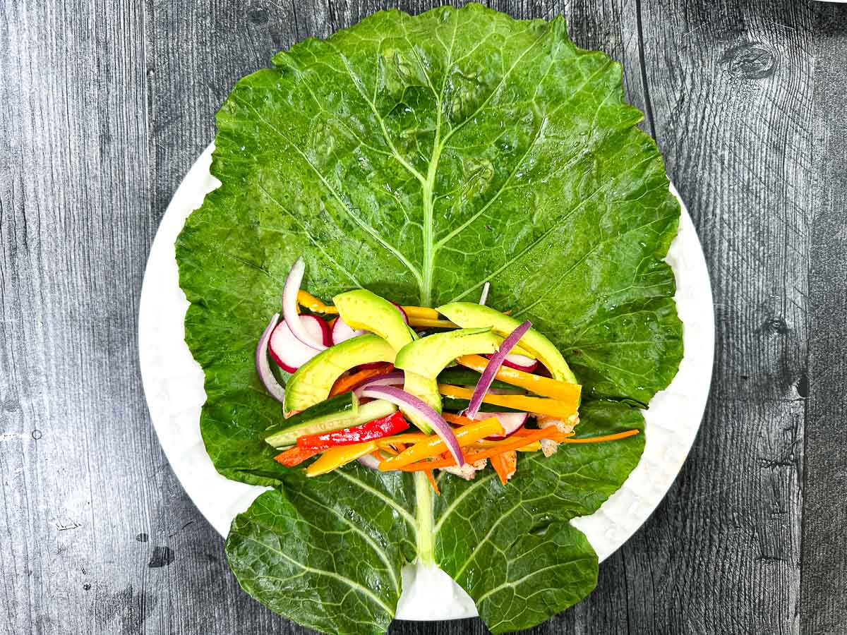 White plate a big collard green on it with all the fixing on it ready to roll up. 