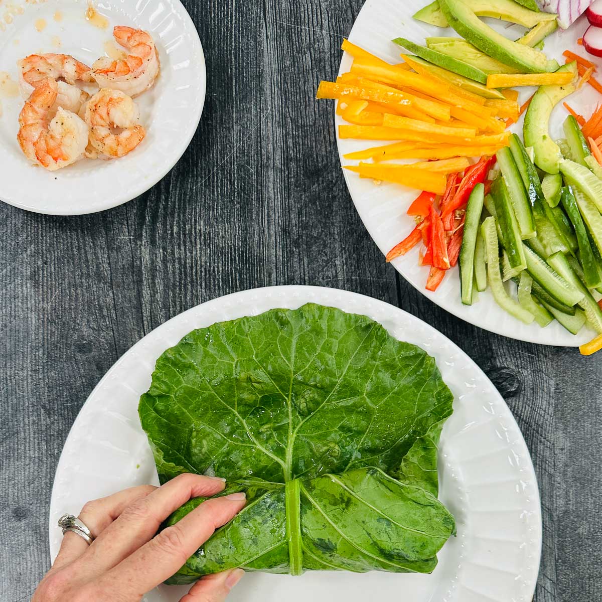 A white plate with a hand rolling up the spring roll with plates of ingredients. 