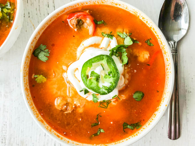 closeup of fajita soup with sour cream, jalapeños and cilantro and a spoon