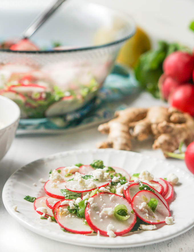 small white plate of radish salad with large glass bowl in background