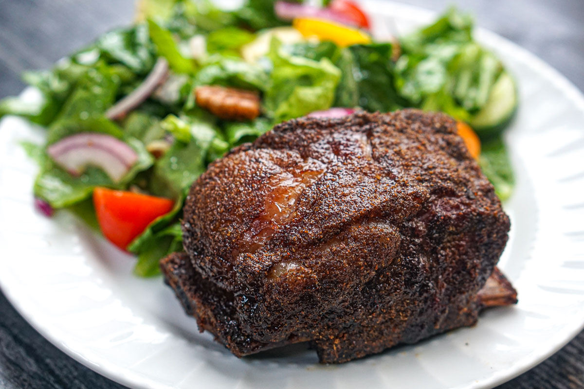 White plate with a bbq smoked short rib and a green salad.