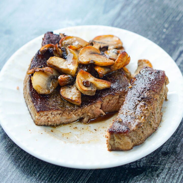 closeup of sous vide round steak on white plate with mushrooms