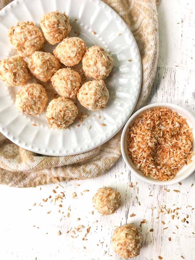 white plate with coconut protein balls and bowl with toasted coconut