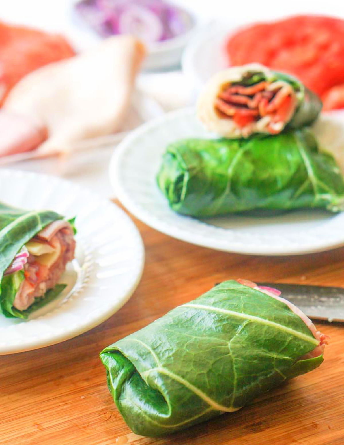 Closeup of green keto collard wraps with sub sandwich filings on white plates.