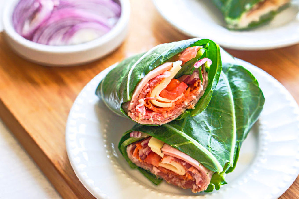 Closeup of a low carb collard wrap sub sandwich on a white plate cut in half.