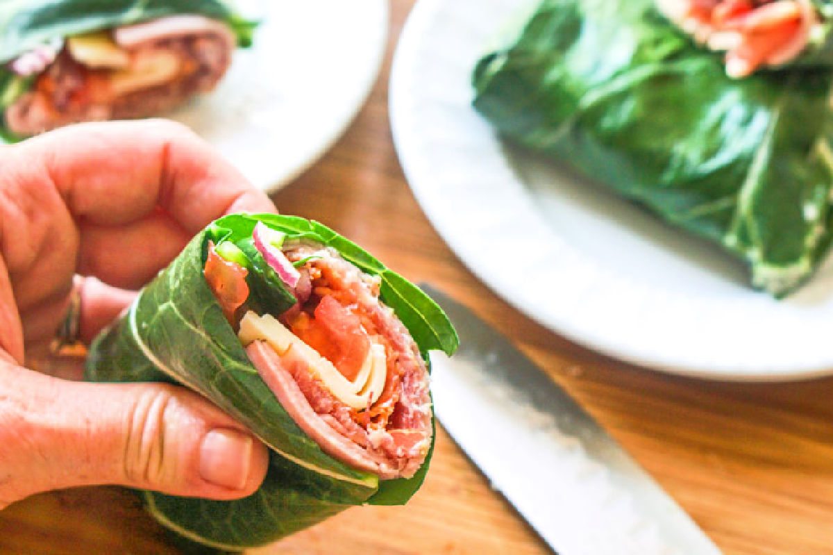A hand holding the sub sandwich wrap using collard leaves.