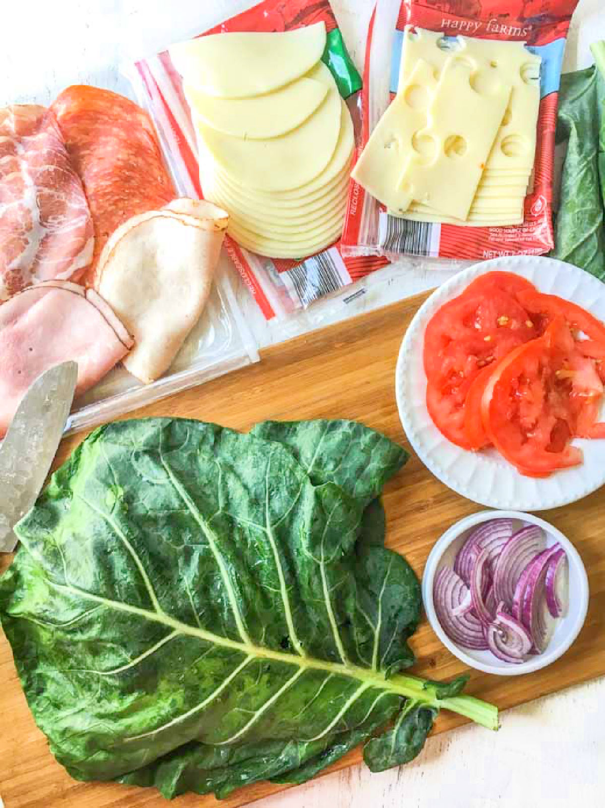 Recipe ingredients - collard green leave, sliced tomatoes, onions, cheeses and deli meats.