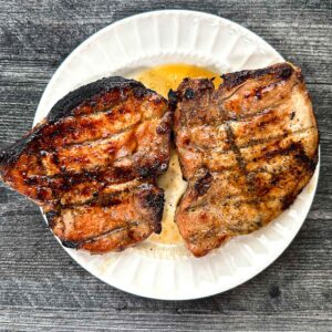 A white plate with 2 keto pork chops glazed and grilled.