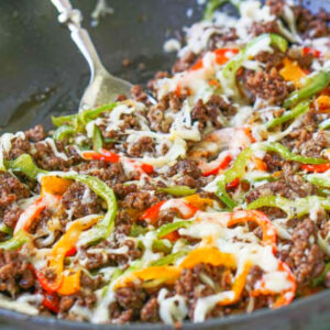 Closeup of a skillet with low carb Philly cheesesteak made with ground beef on a colorful tea towel.