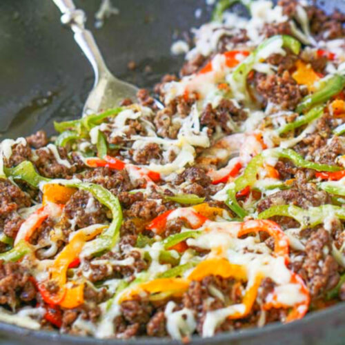 Closeup of a skillet with low carb Philly cheesesteak made with ground beef on a colorful tea towel.