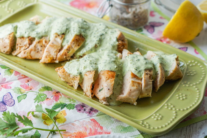green platter with sliced sous vide chicken and low carb creamy herb sauce