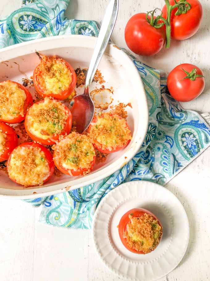 white baking dish and plate with egg stuffed tomatoes on blue towel and few tomatoes on the vine