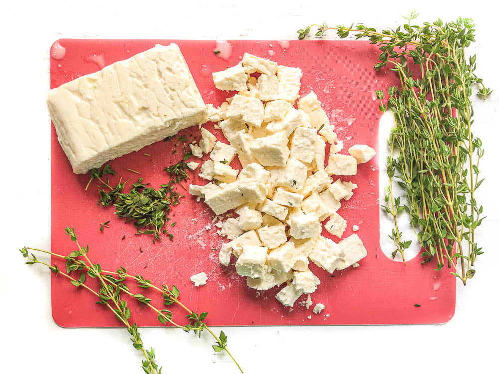 red cutting board with a chunks and a block of feta cheese and fresh thyme sprigs