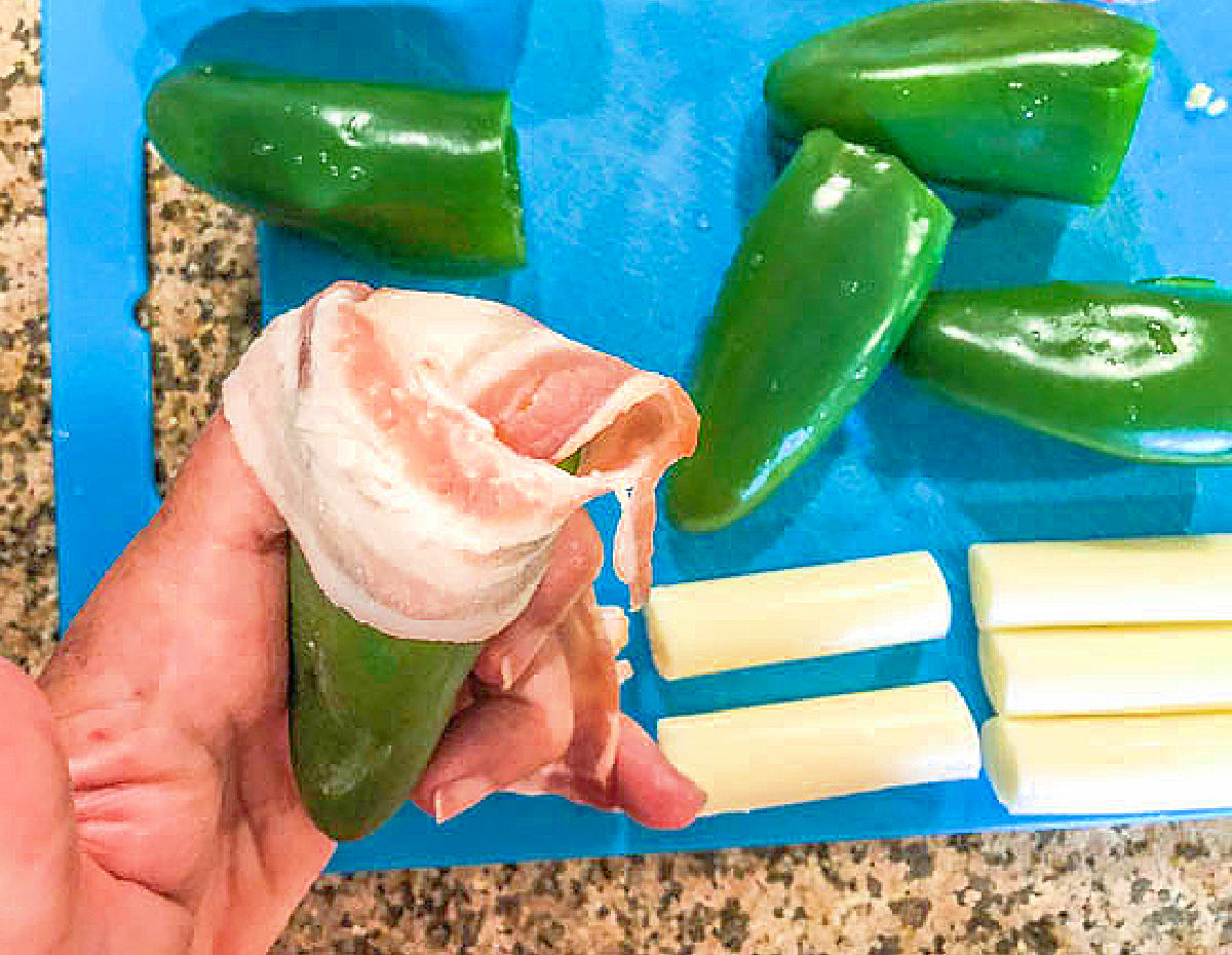 Raw peppers being wrapped in bacon.