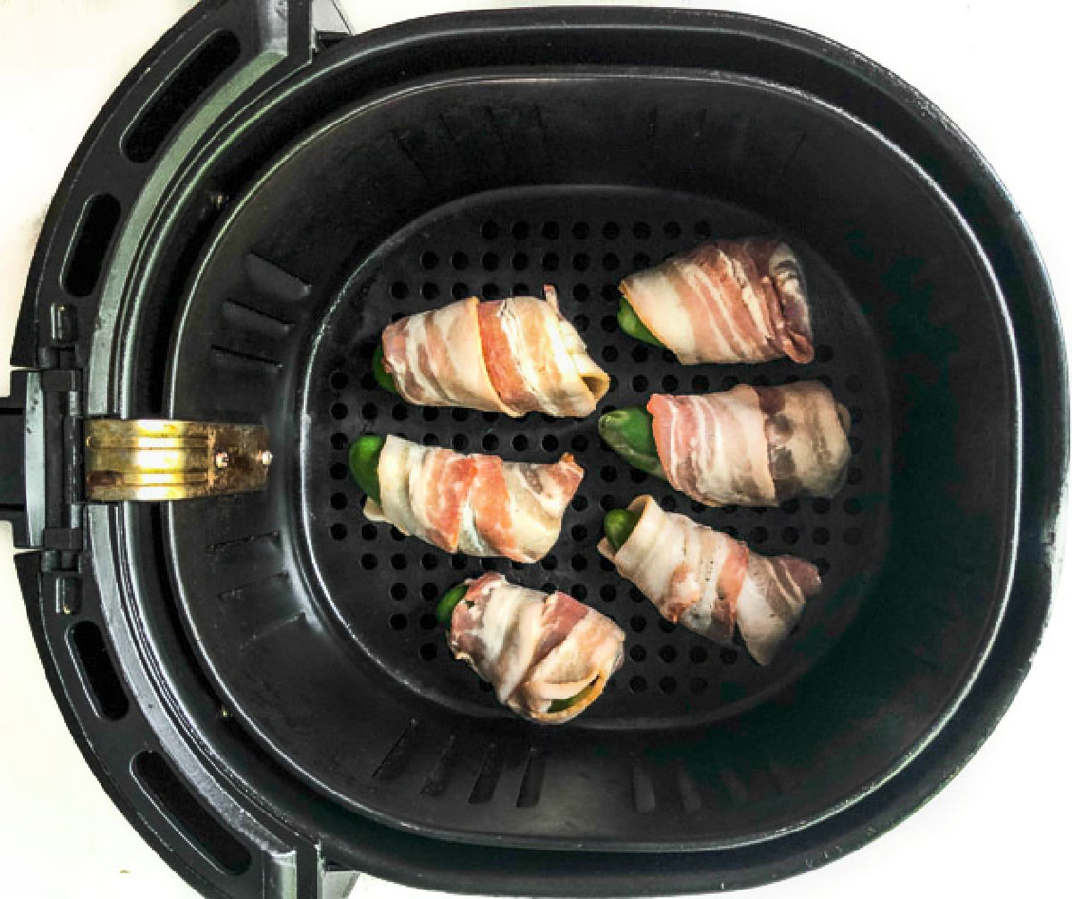 Air fryer basket with the raw wrapped peppers.