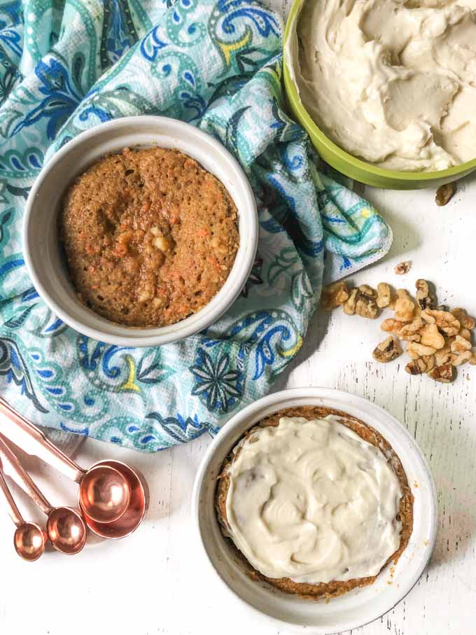 white ramekins with healthy mug cakes with blue tea towel, bowl of frosting , walnuts and copper measuring spoons