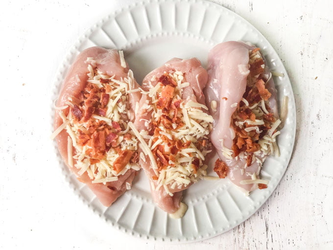 3 raw chicken breasts with cheese and bacon on a white plate
