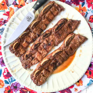 A white plate with 3 grilled short ribs with a Moroccan spice rub.
