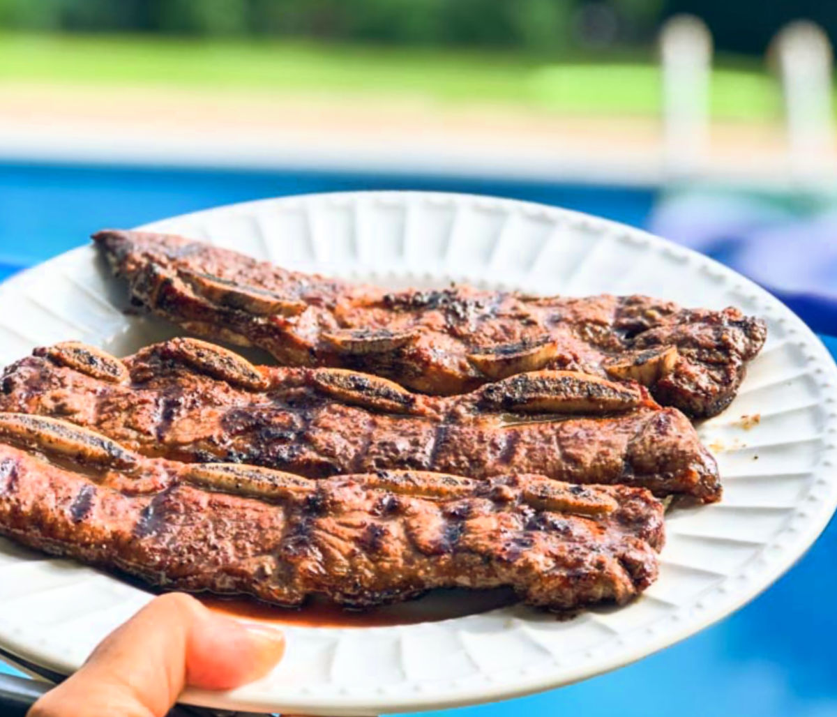 White plate with 3 grilled flanken ribs outside by the pool.