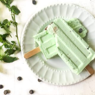 white plate with two mint chocolate chip keto ice pops with fresh mint and chips