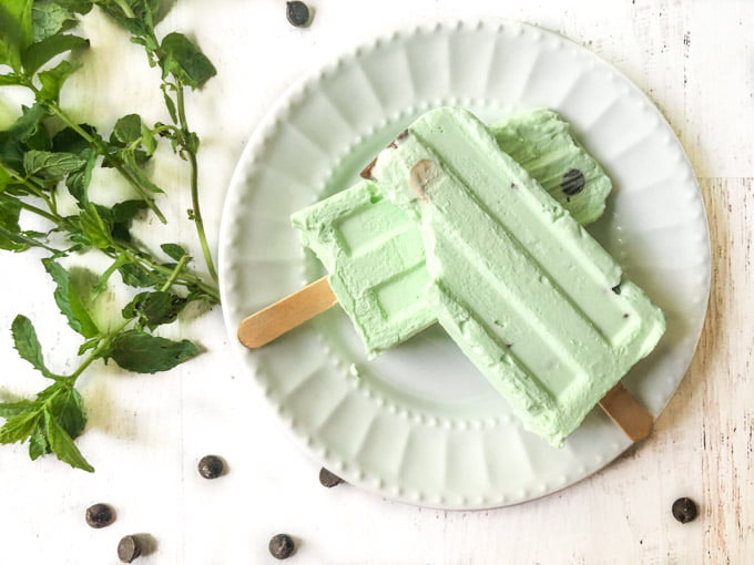 white plate with two mint chocolate chip keto ice pops with fresh mint and chips