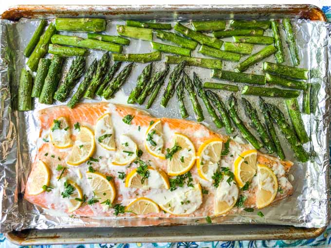 cookie sheet with a whole cooked salmon with lemon slices and asiago sauce and cookie asparagus 