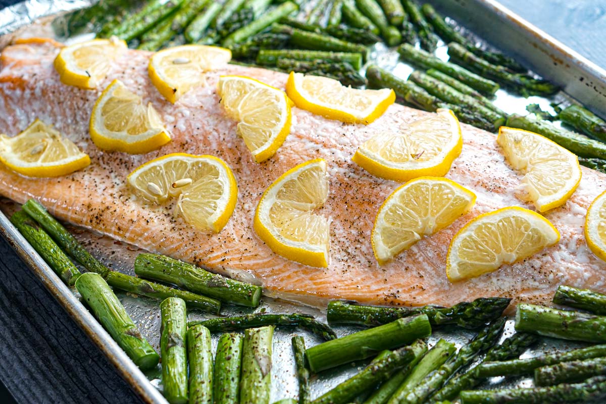 Closeup of a finished salmon covered in lemons and asparagus spears.