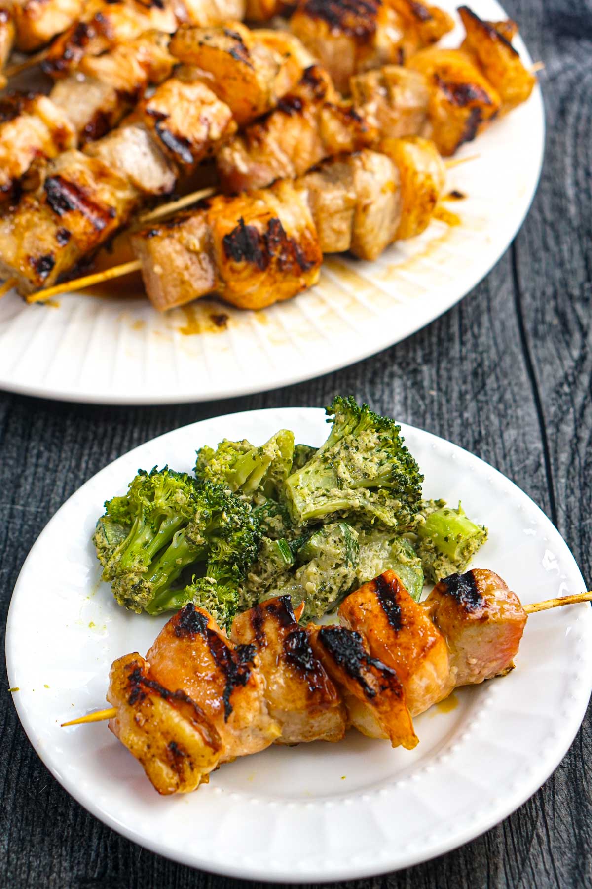 White plate with a seafood kebab and a serving of pesto broccoli  and the platter in the background.