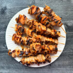 Aerial view of a white plate with marinated and grilled seafood kebabs.