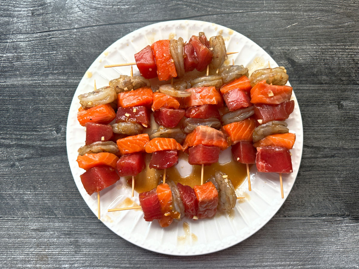 White plate with the raw seafood skewers ready to grill.