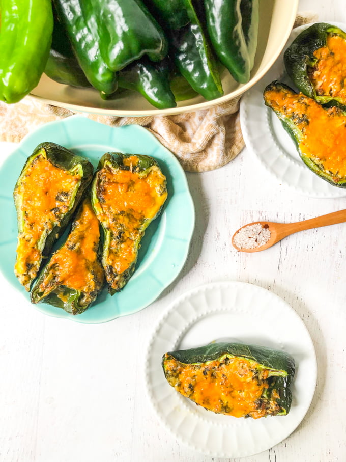 chicken stuffed poblano peppers on white and blue plates with bowl of raw peppers 