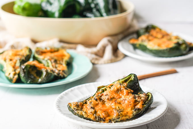 chicken stuffed poblano peppers on white plate with bowl of raw peppers in background