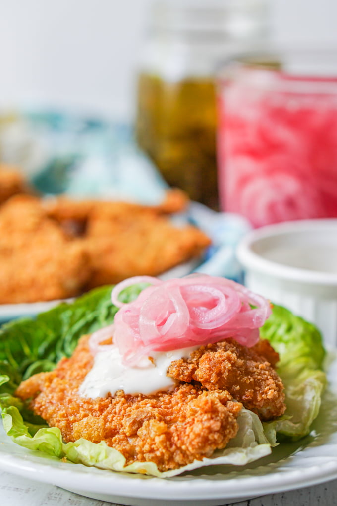 closeup of keto fried chicken sandwich using lettuce as bun with red onion in background
