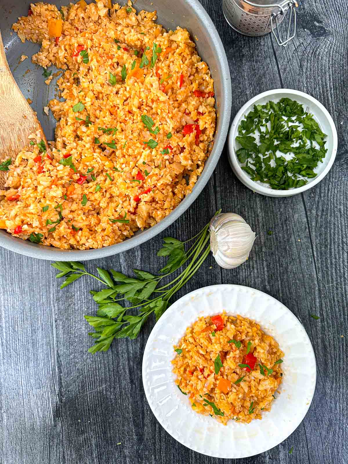 aerial view or pan an white plate with Spanish cauliflower rice and fresh parsley and garlic