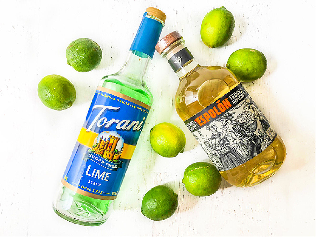 margarita punch ingredients - lime syrup, tequila bottle and limes