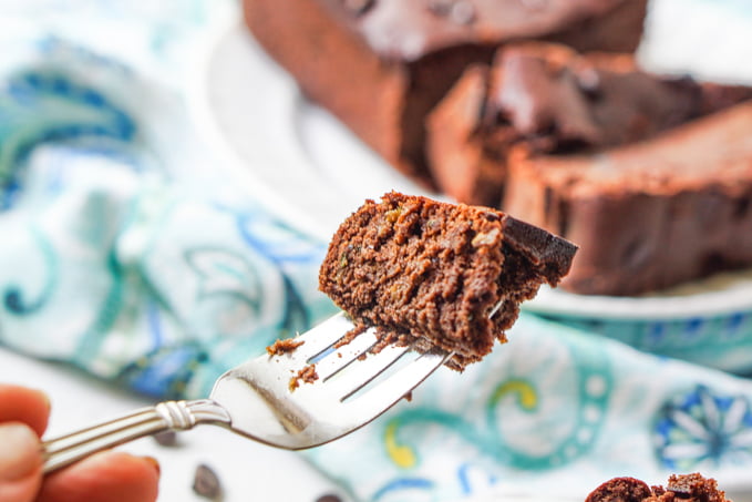 a piece of chocolate zucchini bread on a fork with loaf in background on blue tea towel