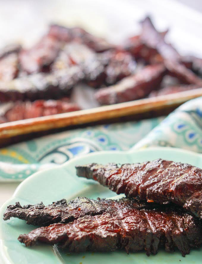 blue plate with low carb smoked beef jerky and a cookie sheet full of jerky in background