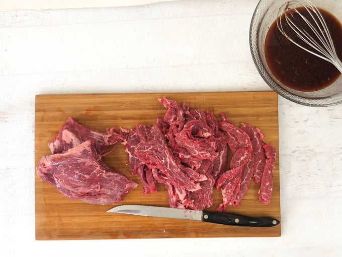 raw flank steak cut into beef jerky strips on a wooden cutting board with knife 