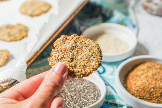 hand holding homemade round cracker with seeds in background