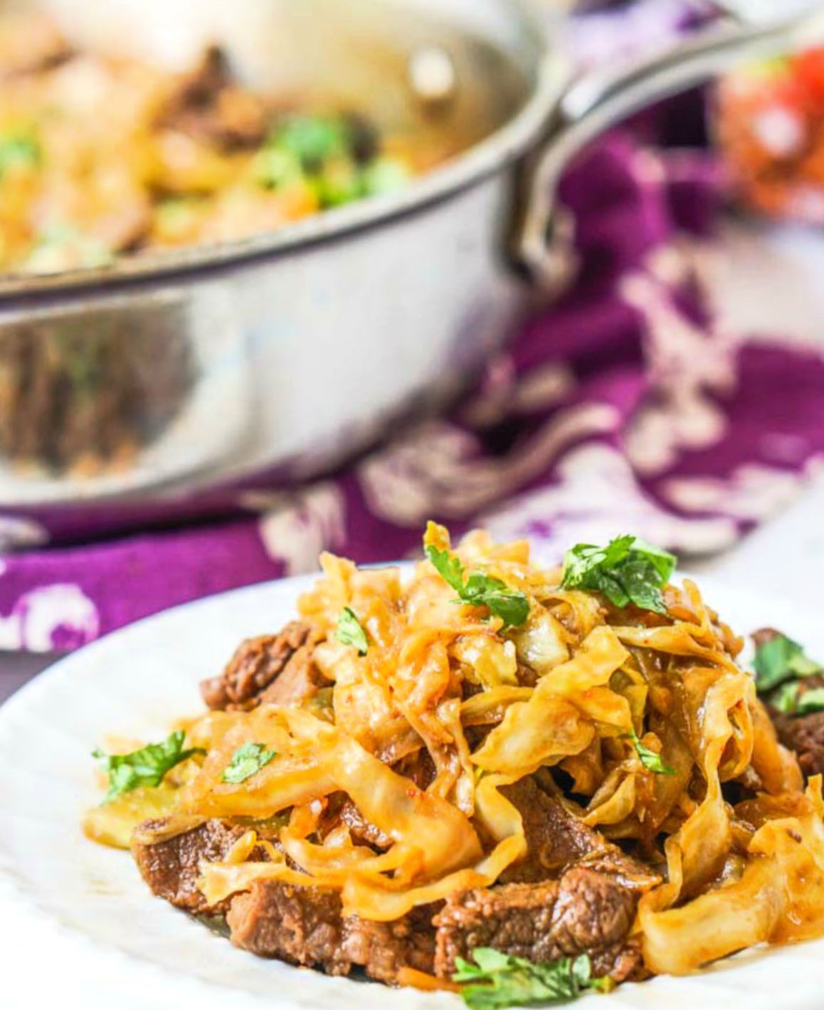 Closeup of a white plate with Asian low carb beef and cabbage stir fry and pan in the background.