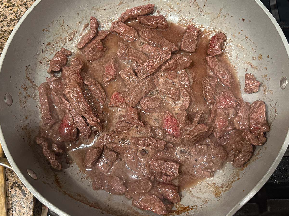 Skillet with strips of beef being browned.
