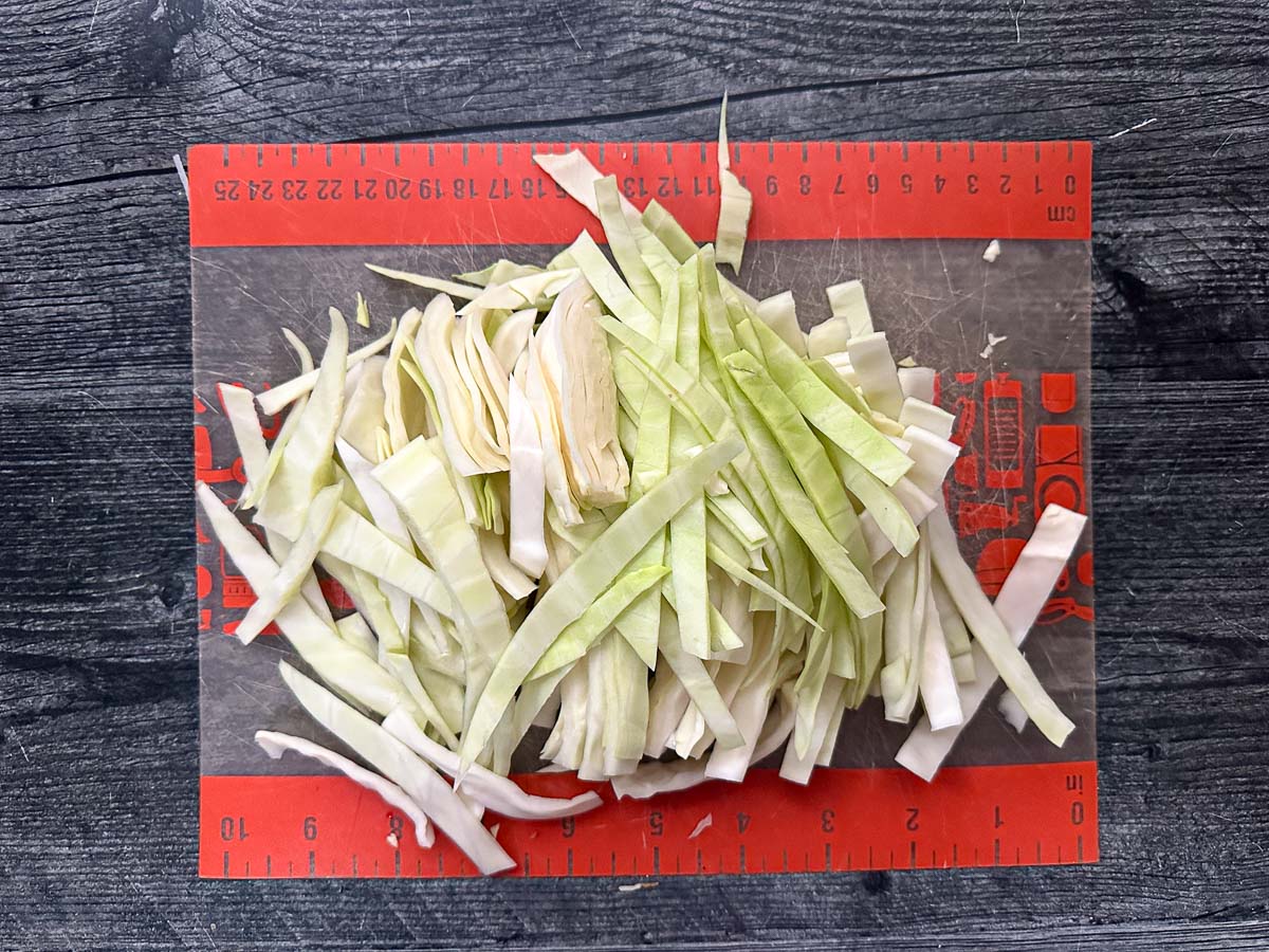 Cutting board with strips of green cabbage.