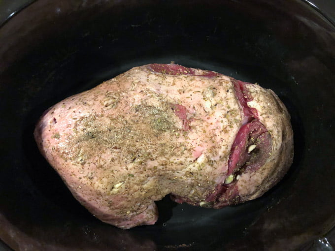 garlic studded lamb roast with spices rubbed on in a slow cooker crock