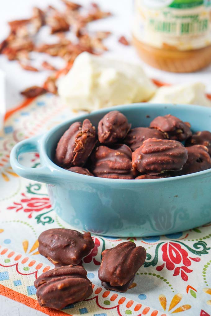 blue bowl with low carb chocolate covered pecans on printed napkin with peanut butter in background