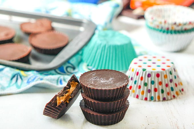 low carb peanut butter cups stacked with cupcake liners and a tray of candy in background